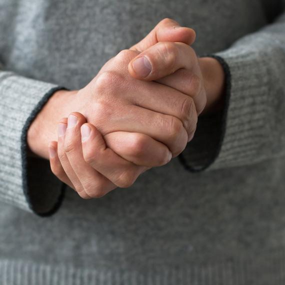 Nahaufnahme von gefalteten Händen einer Person in einem grauen Pullover.
